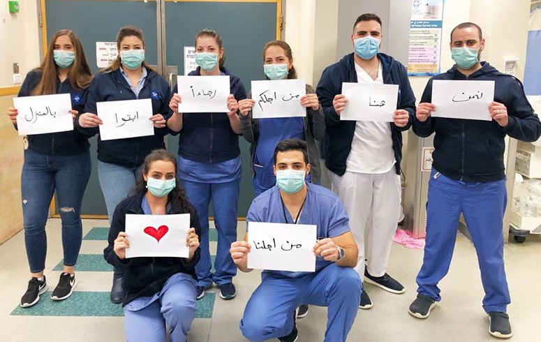 Medical staff holding signs that say "We are at Work for You" in Arabic